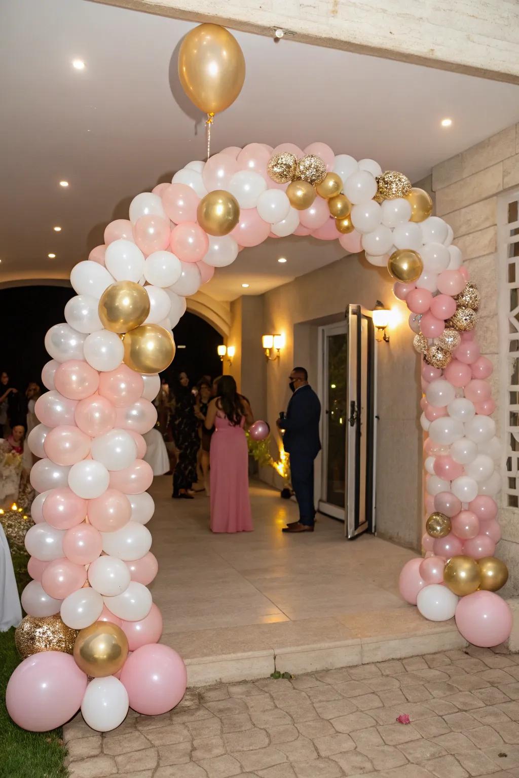 A stunning balloon arch in pink, gold, and white welcomes guests.