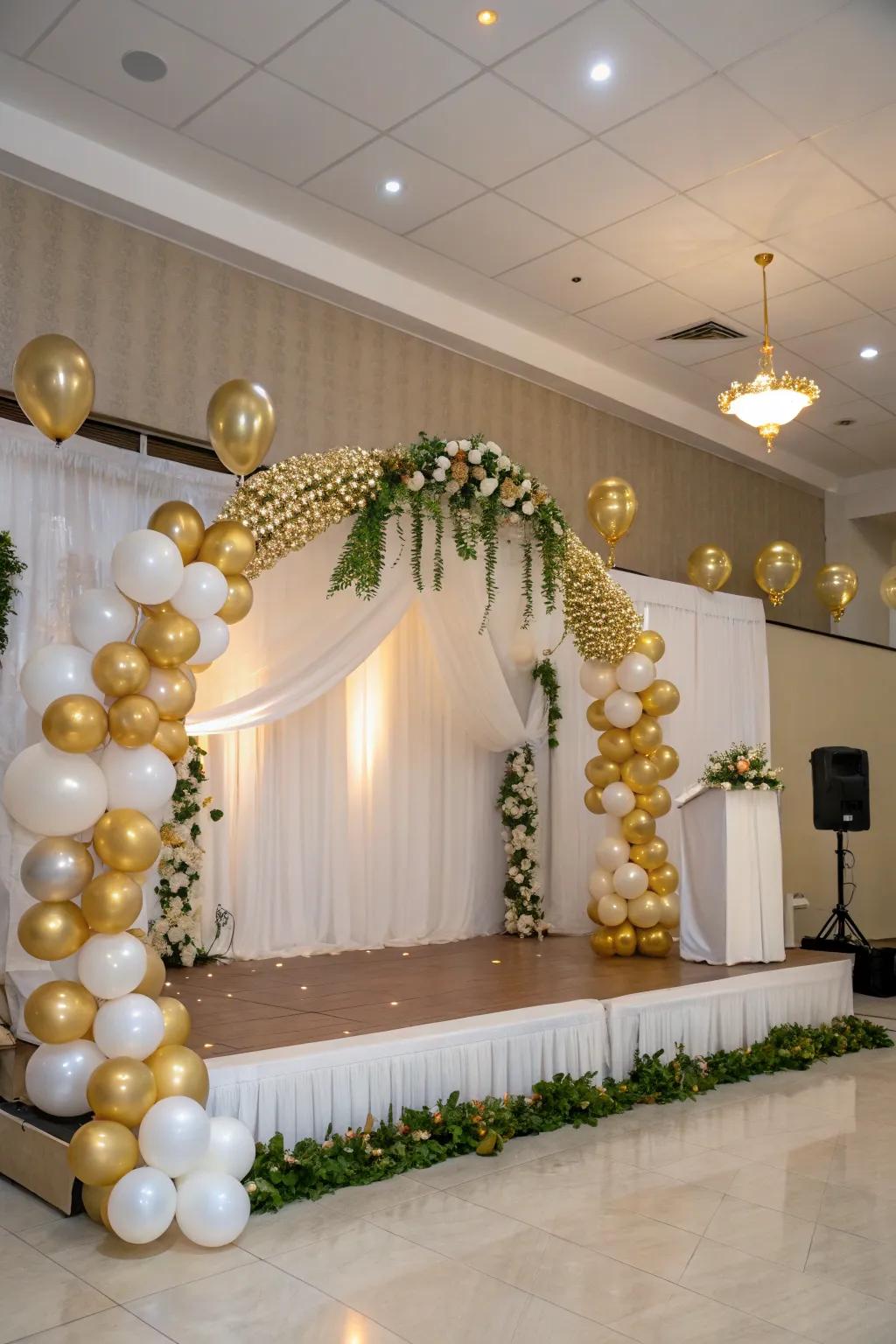 A sophisticated balloon arch and festoon in gold and white, framing the stage beautifully.
